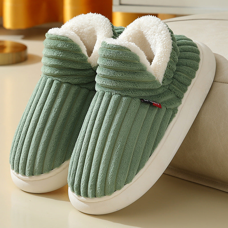 Green plush winter slippers with fleece lining and anti-slip soles on a beige surface.