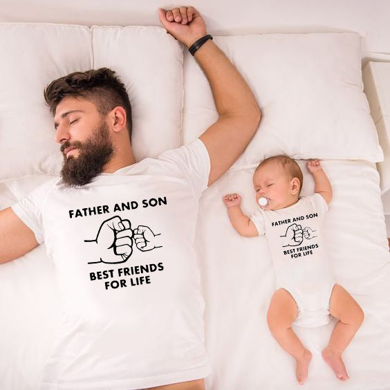 Father and son wearing matching "Best Friends for Life" outfits, lying on a bed. Both in white, cotton parent-child wear.